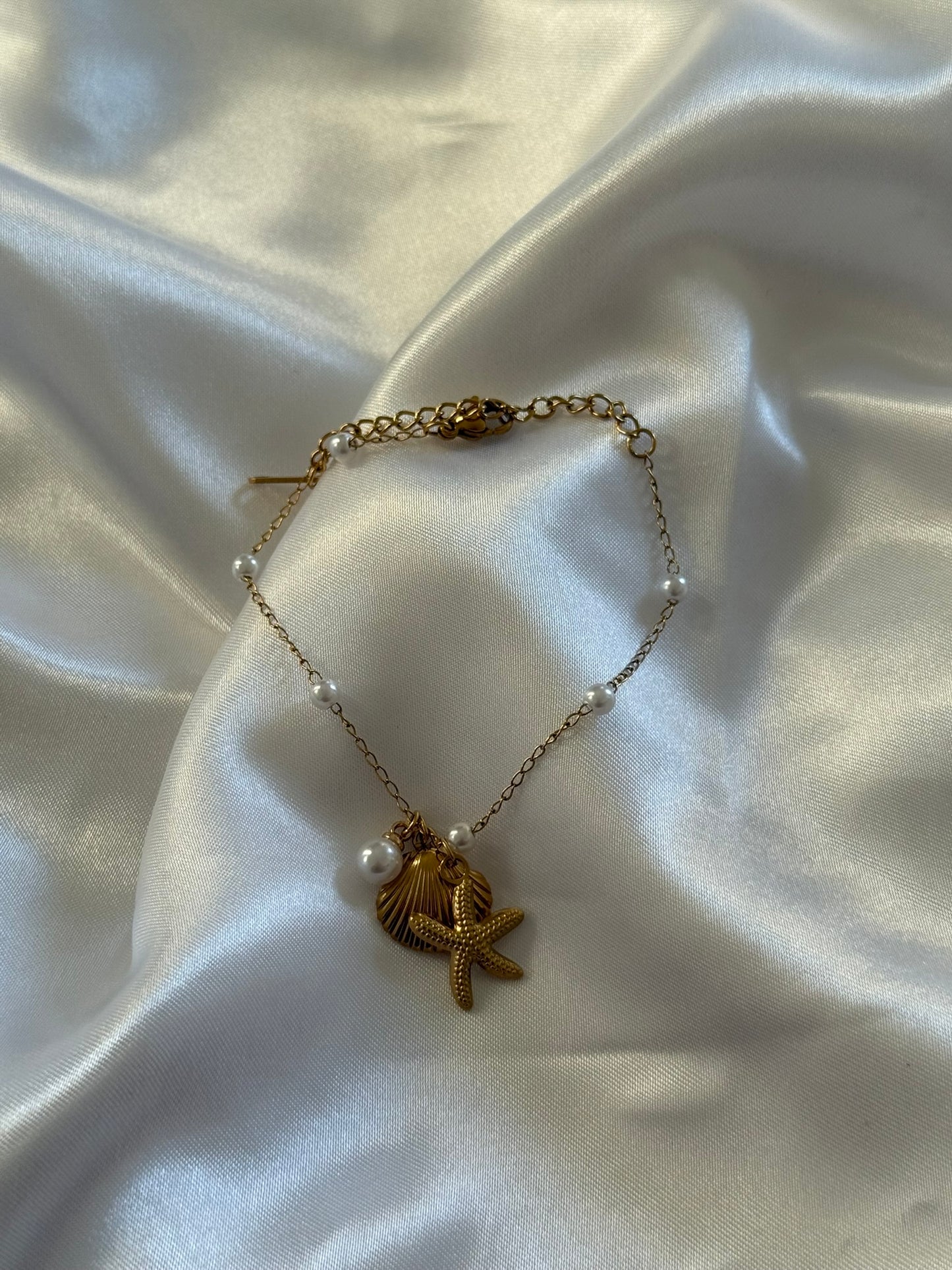 Bracelet Marina en acier inoxydable doré avec détails coquillages, étoile de mer et perles sur fond blanc satiné - Onaïa Bijoux