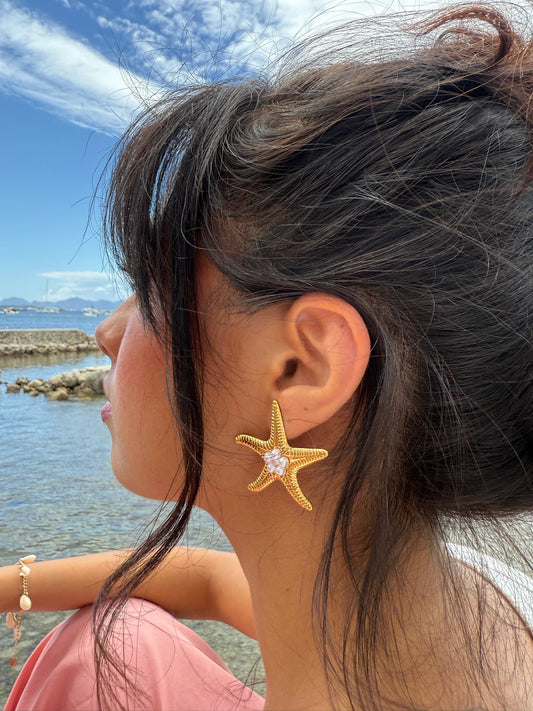 Boucles d'oreilles Stellina en acier inoxydable portées par une jeune femme en bord de mer - Onaïa Bijoux