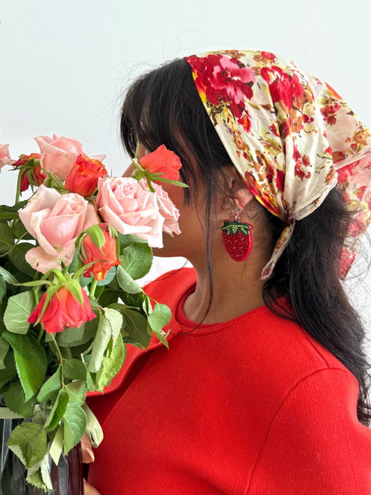 Jeune femme portant les boucles d'oreilles fragaria en perle avec une tenue colorée et un bouquet de fleurs 