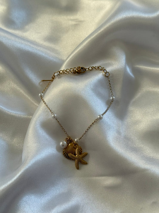 Bracelet Marina en acier inoxydable doré avec détails coquillages, étoile de mer et perles sur fond blanc satiné - Onaïa Bijoux