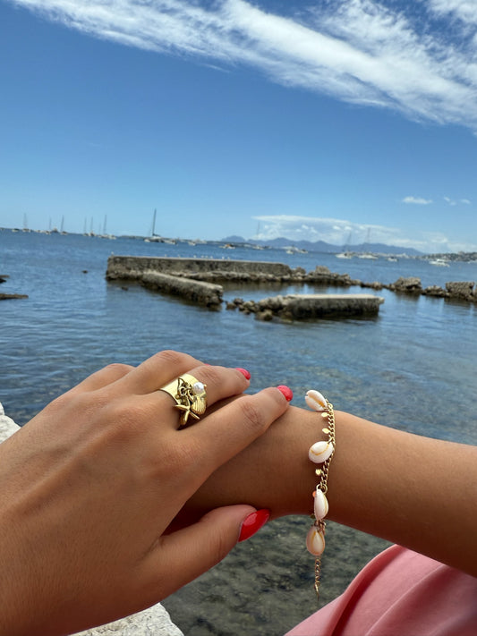 Bracelet doré Isla en acier inoxydable, orné de coquillages blancs, porté en bord de mer pour un look estival raffiné signé Onaïa Bijoux.