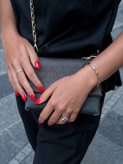 Duo de bagues dorées Solaris, bracelet doré Sardina et bague argentée Fiorina signés Onaïa Bijoux, portés avec une tenue noire et un sac chic.
